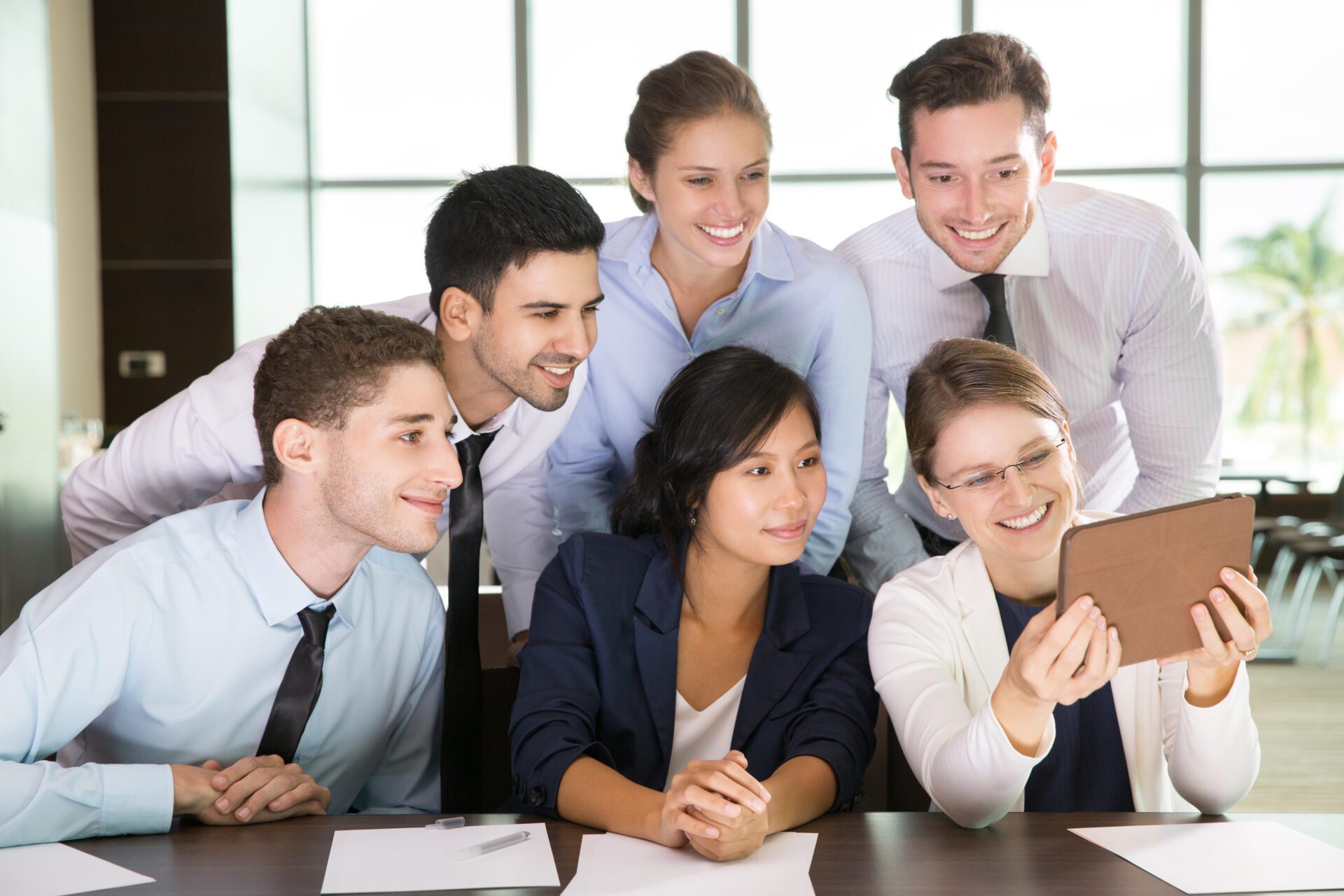 Group of six business people discussing business ideas and smiling. Female executive manager sitting at office desk and showing something on tablet computer to business team. Team concept